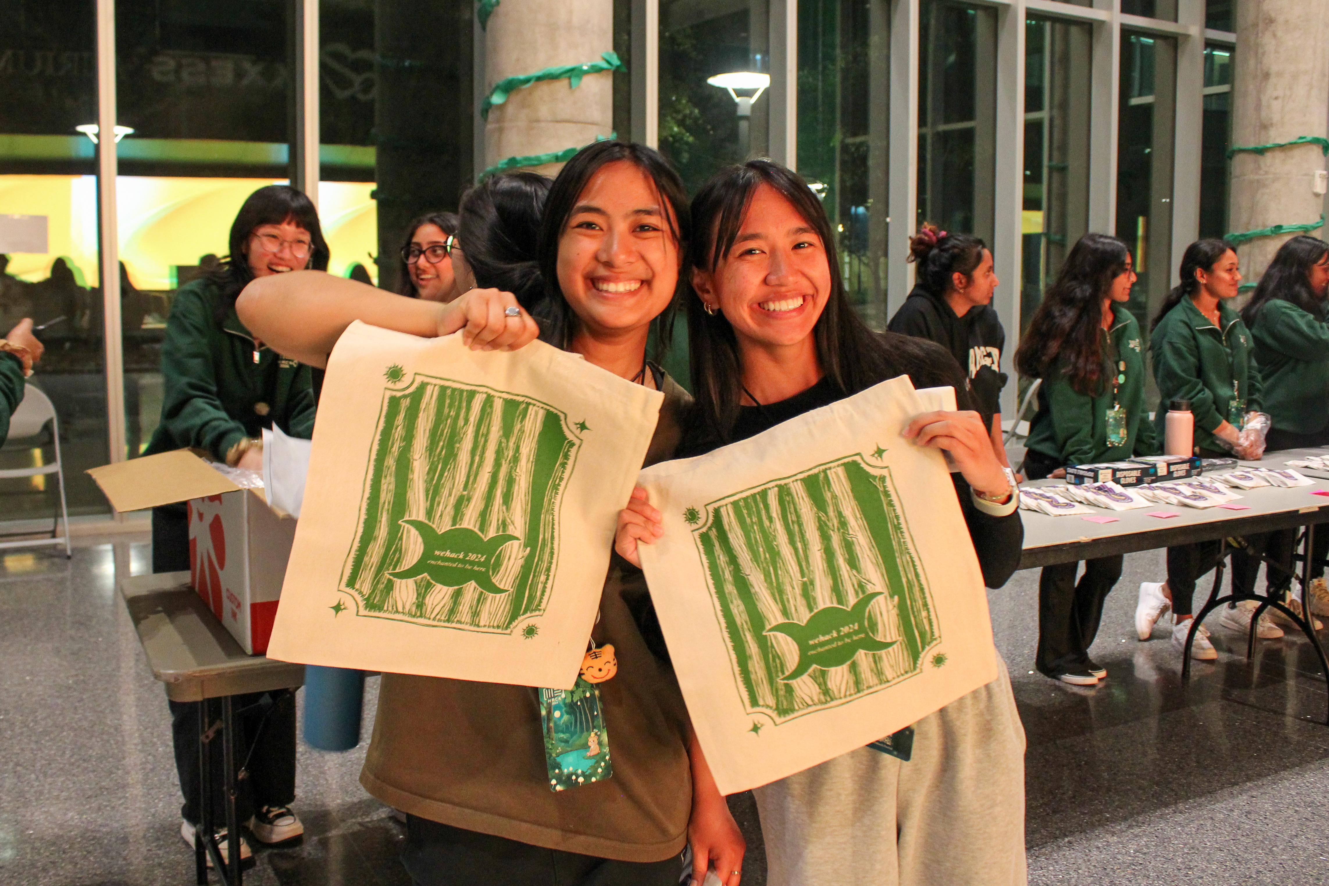 two girls smiling at the camera, holding a WEHack tote bag